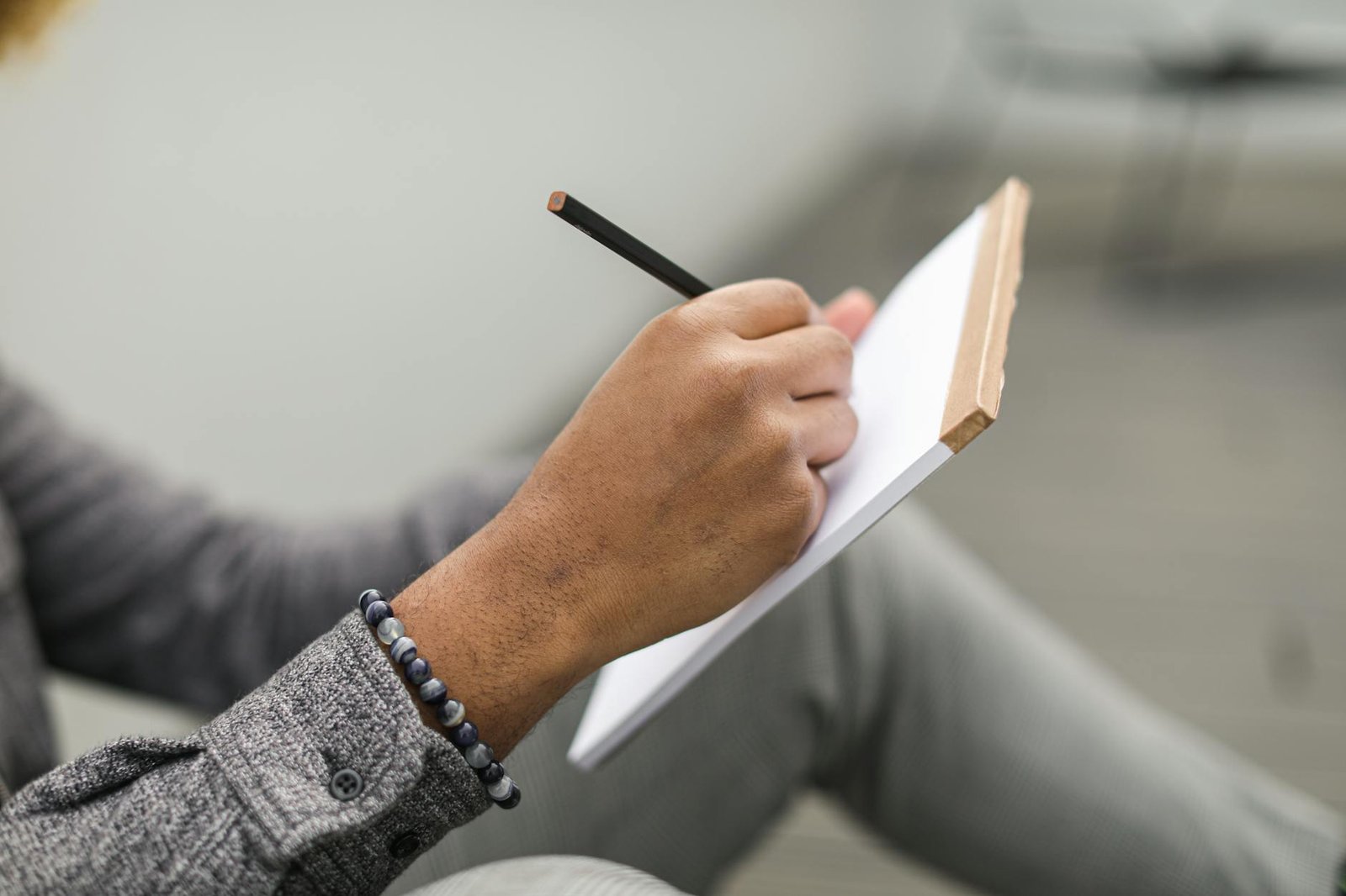 Mani che scrivono su un quaderno con una tazza accanto, in atmosfera tranquilla